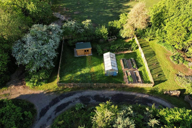 Blick aus der Vogelperspektive auf einen naturnahen Garten in der Abendsonne, mit Gewächshaus, Hochbeeten, Gartenhaus