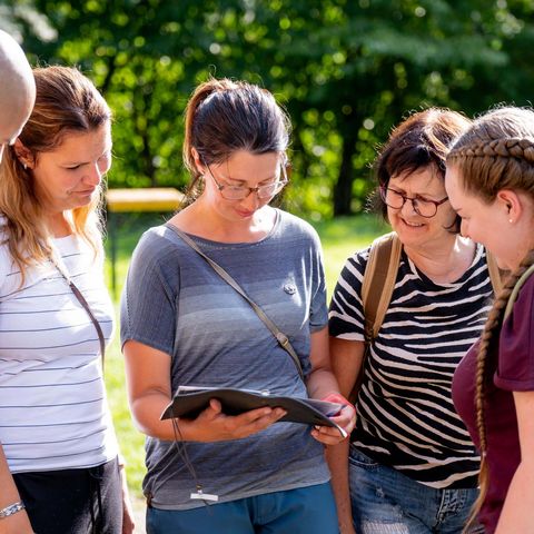 Personengruppe betrachtet gemeinsam eine Kladde, eine Frau liest daraus vor