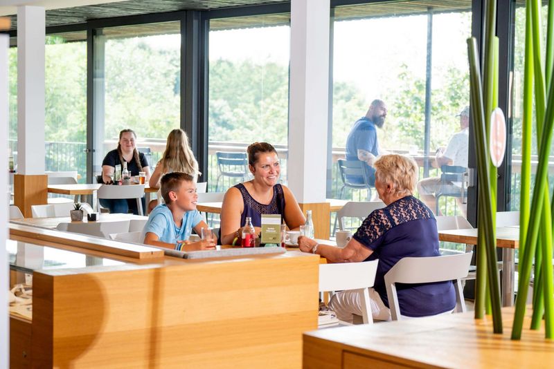 Lächelnde Menschen sitzen an Cafétischen im Hintergrund eine sonnige Terrasse